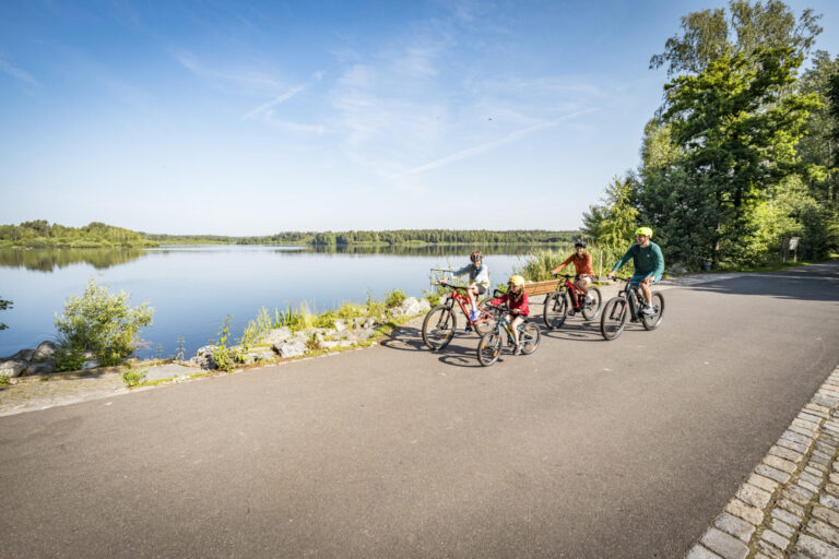 Familie beim Radfahren am Rußweiher; im Hintergrund Rußweiher